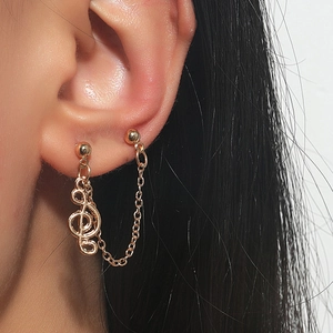 Close-up of golden music note earring set with delicate metal chain and sphere studs