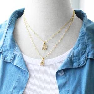 Close-up of gold layered initial necklaces with zircon micro-pave letters A and B