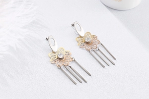 Détail de boucles d'oreilles pétales ajourés avec de longs pompons et strass brillants