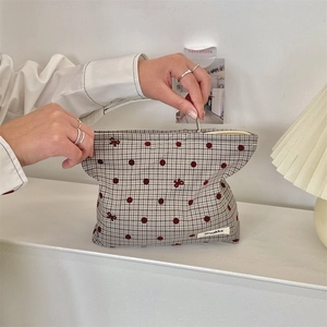 Dettaglio della trousse a quadretti con pois rossi e ricamo a fiocco in mano