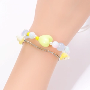 Detalle de pulsera de doble capa con cuentas pastel, corazón amarillo y cadena de plata