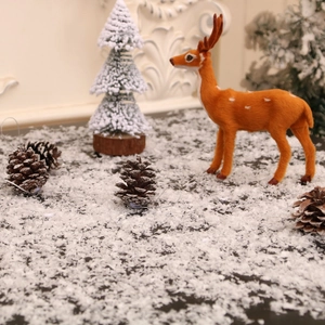 Artificial snow scene with orange deer and mini Christmas trees for festive holiday decor