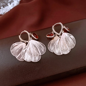Detail of silver hoop earrings with radial petal motifs and dark red teardrop gemstones