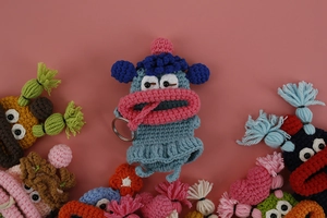 Close-up of handmade crochet monster key cases in multiple vibrant colors on pink background