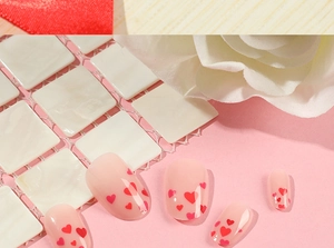 Detailed view of pink press-on nails with red heart patterns and floral decor
