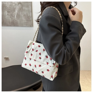 Detail showing white corduroy shoulder bag with red strawberry pattern and gold chain