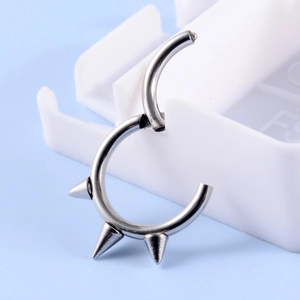 Close-up of silver steel ring with three cone spikes on a white tray with blue background