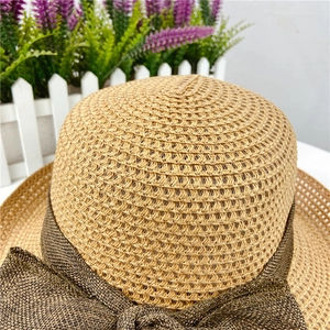 Detailed texture of woven straw sun hat with a large brown ribbon bow on white fence