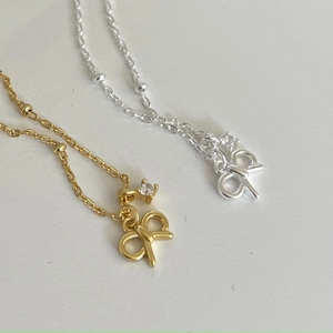 Detailed view of silver and gold bow pendant necklaces with zircon stone accents