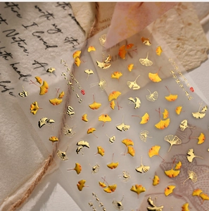 Macro shot of ginkgo leaf nail stickers with gold foil details and autumn poetry text