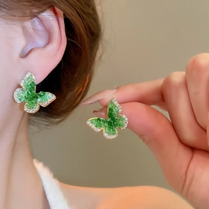 Detailed close-up of 18k gold butterfly earrings with green stones and sparkling crystals