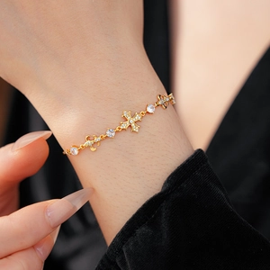 Détail d'un bracelet doré avec pendentif croix, fleur et zircons blancs sur un poignet