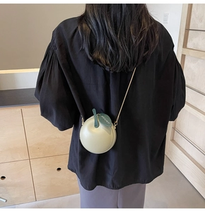 Detail of light green apple-shaped crossbody bag with gold chain strap on a model