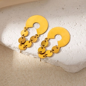 Close-up of golden titanium steel earrings with irregular round pendants on white stone