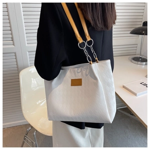 Close-up of a white quilted tote bag with yellow shoulder strap in a modern office setting