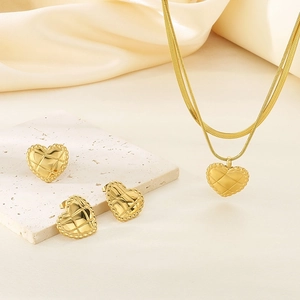 Detail of 18K gold plated heart jewelry set with quilted texture on beige silk background