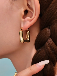 Close-up of polished gold U-shaped earrings on model ear against blue background