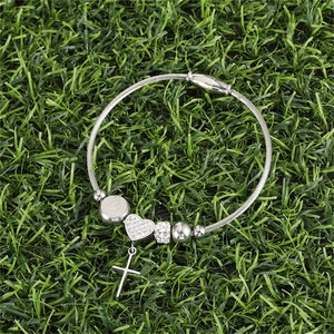 Detail of silver steel wire bracelet with crystal heart and cross charms on grass