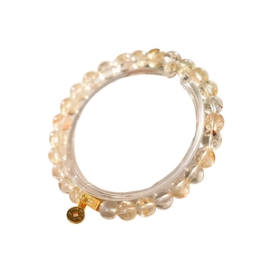 Golden rutilated and clear quartz beaded bracelet with a lucky coin charm on a white base