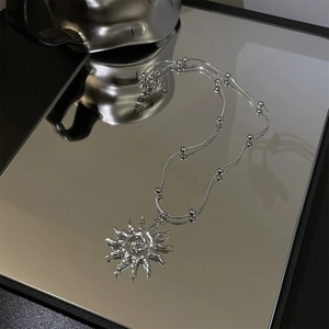 Silver layered necklace with hollow sun pendant and beaded chains on reflective surface