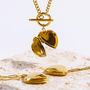 Detailed view of open and closed gold heart locket necklaces on a textured stone block