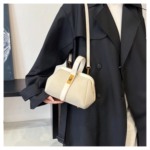 Detail of cream shell bag with golden twist lock and matte texture on black coat background