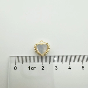 Detail view of 18K gold-plated heart pendant with white shell inlay next to a metric ruler