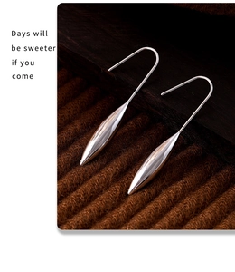 Macro view of silver water drop earrings on a dark wood and striped fabric background