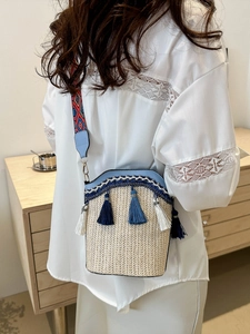Detailed view of beige woven bucket bag with blue leather trim and colorful wide strap