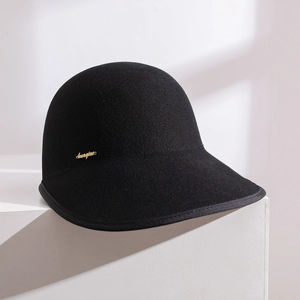 Retro black wool felt equestrian cap with gold metal logo on a clean white stone base