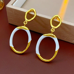 Detail of gold and white enamel irregular oval hoop earrings on leather surface