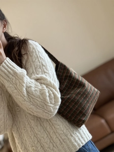 Close-up of retro plaid woolen handbag styled with a cream cable knit cardigan sweater