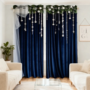 Detail of dark blue velvet blackout curtain with decorative white pom-poms and greenery