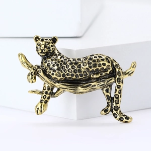 Golden leopard brooch with black spots on tree branch against clean white background