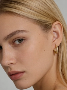 Detailed close-up of a gold-toned textured surface earring worn by a female model