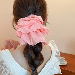 Detailed back view of a pink ruffled fabric scrunchie on a ponytail in elegant setting