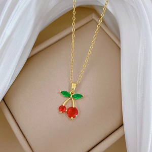 Elegant gold chain necklace with sparkling red cherry pendant on luxury beige tray