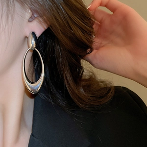 Close-up of a silver oval hollow drop earring worn by a model with a metallic finish