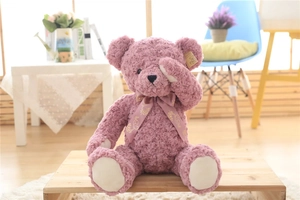 Detail of mauve rose-textured plush teddy bear with silk bow on a wooden stool