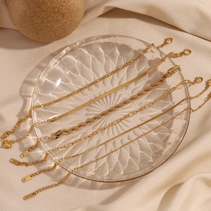 Macro shot of 18K gold plated Figaro and snake chain bracelets on textured glass tray