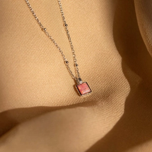 Macro view of square pink opal pendant on a silver beaded chain over gold fabric