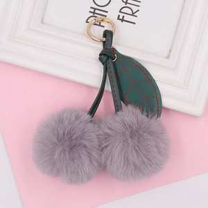 Close-up of gray faux fur cherry plush keychain with green faux leather leaf and gold ring