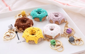 Macro detail of five handmade knitted donut keychains with colorful bells on white plate