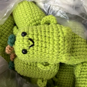 Handmade green crochet dinosaur plushies inside white plastic shipping bags