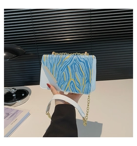 Detail of blue and white crossbody bag with yellow line embroidery on the flap cover