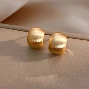 Minimalist golden geometric C-shape stud earrings with brushed matte finish on beige fabric