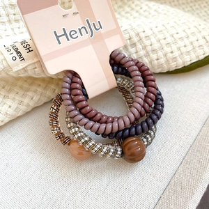 Macro detail of five spiral telephone wire hair ties with beads on a branded display card