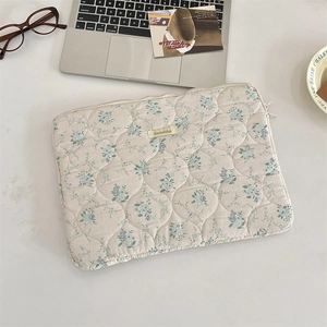 Macro view of quilted floral laptop sleeve featuring delicate blue embroidery and soft fabric