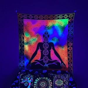 Glow-in-the-dark chakra tapestry with meditating figure and nebula under UV blacklight