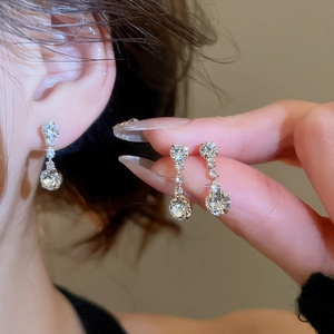 Detail of silver tassel earrings with sparkling rhinestones worn on ear and held by hand